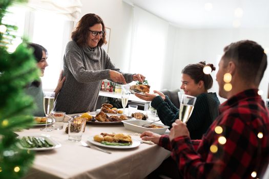 Happiness at home for Christmas. Smiling caucasian family have Christmas meal together. Mother serves daughter roasted chicken. Holiday concept.