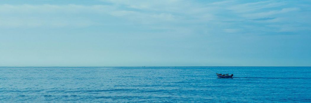 Simple background Calm dark blue sea fishing boat alone white pale Spindrift clouds Open way no limitations. BANNER LONG FORMAT.