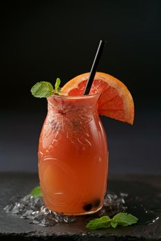 Grapefruit juice in a glass jar with pieces of fruit on a wooden table, selective focus