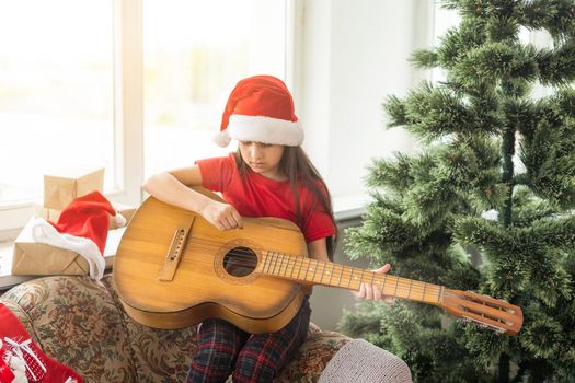 Happy little girl in red hat playing the on the background of christmas tree. Talent kid having fun on winter holidays at cozy decorated home