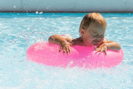 A small child swims in a pink swimming circle in the pool close up