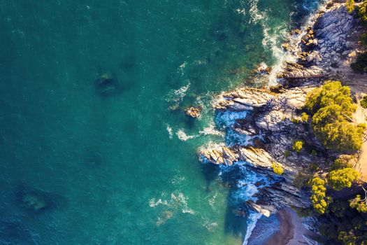 aerial top view of turquoise ocean with sea waves crashing on the rocky island coast with spray and foam, concept of adventure lifestyle and summer holidays in the wilderness