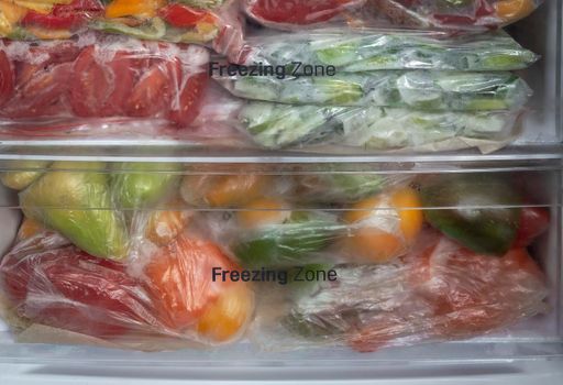 Sliced cucumbers, tomatoes, bell peppers are stored frozen in cellophane bags in the freezer of the refrigerator. Front view, close-up.
