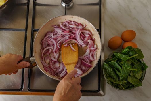 top view of a woman pouring shallot onion into a pan with boiling oil