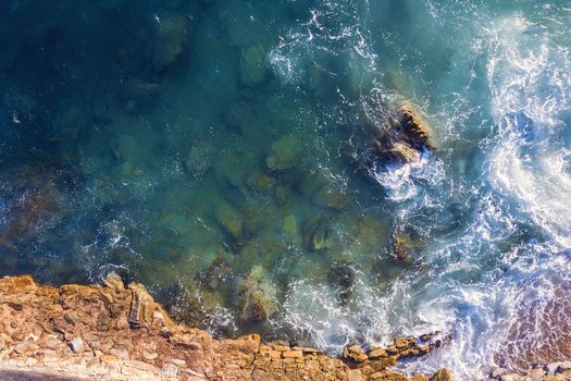 top view of sea waves hitting on the seashore of the rocky coast with spray and foam, power of the nature concept