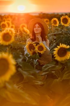 A girl in a hat on a beautiful field of sunflowers against the sky in the evening light of a summer sunset. Sunbeams through the flower field. Natural background