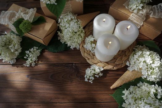 Beautiful still life with hydrangeas and ice cream cones. The summer sun illuminates the florist's table. Three lighted candles are burning on the table.