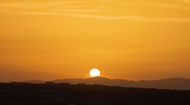 Big sun on sunset hiding behind mountains. Golden coloured sky