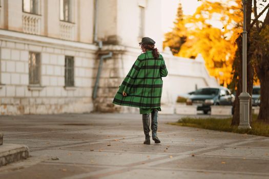 Outdoor fashion portrait of an elegant fashionable brunette woman, model in a stylish cap, green dress, posing at sunset in a European city in autumn