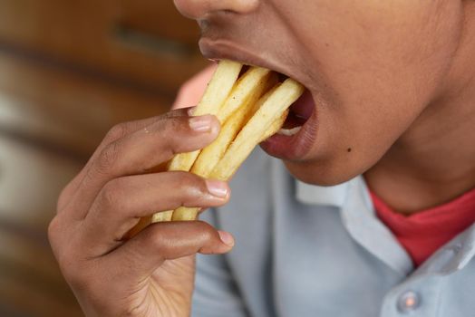 a teenage boy eating french fries while sited .