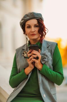 Outdoor fashion portrait of an elegant fashionable brunette model in a beret, green dress and a gray waistcoat posing at sunset in a european city in autumn