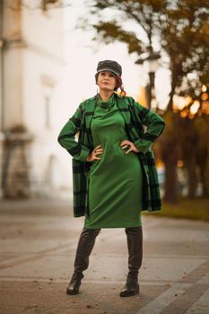 Outdoor fashion portrait of an elegant fashionable brunette woman, model in a stylish cap, green dress, posing at sunset in a European city in autumn