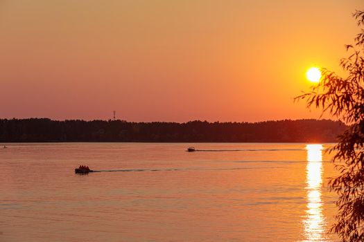 A boat pulls a person over the waves on a wakeboard. Wakeboarding at sunset.