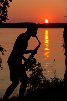 Silhouette of a young guy playing the saxophone in the evening at sunset.