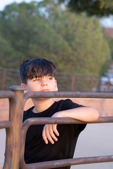 Portrait of handsome boy focused looking at sunset. Teenager with thoughtful expression relaxed with his arm on a vintage steel railing. Looking ahead concept