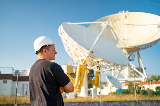 Engineer looking earth based astronomical radio telescope. Radio telescopes used in science for space observation and distant objects exploring. Caucasian man white protective helmet satellite dishes