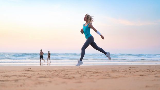 Active sporty woman run along ocean surf by water pool to keep fit and health. Sunset sand beach background with sun. Woman fitness, jogging workout and sport activity on summer family holiday.
