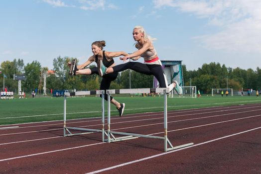 Two athlete woman runnner running hurdles at the stadium outdoors