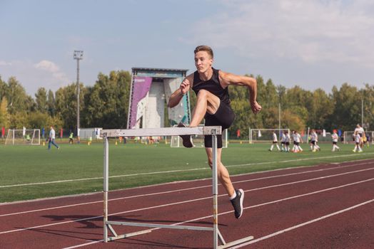Young man athlete runnner running hurdles at the stadium outdoors