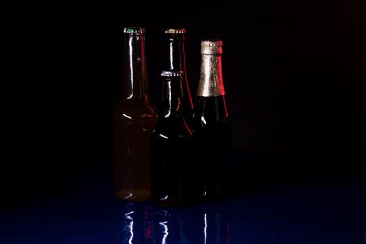 silhouettes of four beer bottles on a black background, set on a blue shiny surface.