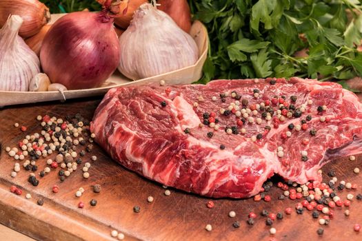 steak of beef on a wooden board with spices pepper parsley salt onions shallots garlic