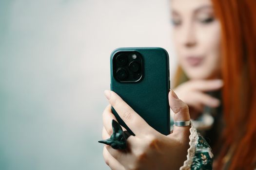 Attractive woman fashion blogger takes selfie on iPhone 13 pro. Female's hand with black gothic rings holding smartphone in case. Gadget with triple-lens camera. Bishkek, Kyrgyzstan - January 24, 2022