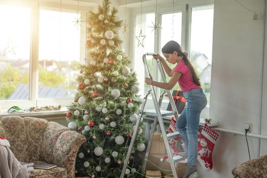 Cute little girl decorating Christmas tree on background.