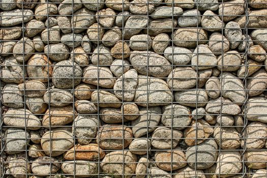 Wall made of round rocks, secured with steel wire net (iron stone gabion)