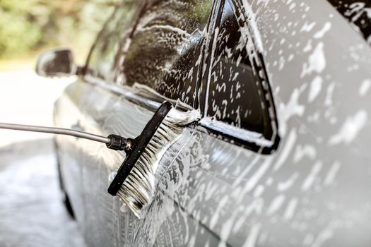 Side of silver car washed in self service carwash, brush leaving strokes in shampoo and foam.