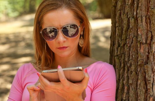 Young woman in sunglasses, sitting on a bench in park, working with tablet. Detail on her head.