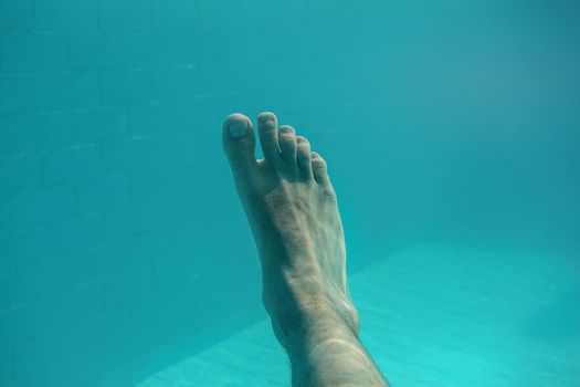 Underwater photo - man's single foot with light blue swimming pool tiles in background.