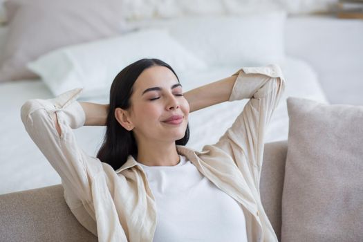 A young beautiful female student is resting, napping on the sofa at home after studying, after the exam. She closed her eyes, threw her hands behind her head, relaxed.