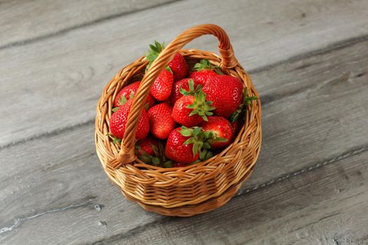 Basket full of freshly picked strawberries on gray wood desk.