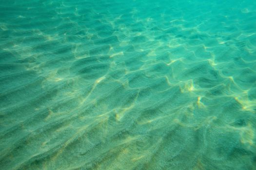 Ocean floor underwater photo, sand "dunes" lit by sunlight. Abstract marine background.