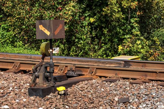 Old railway cross switch covered with black oil and dirt. Rail tracks and green bushes in background.