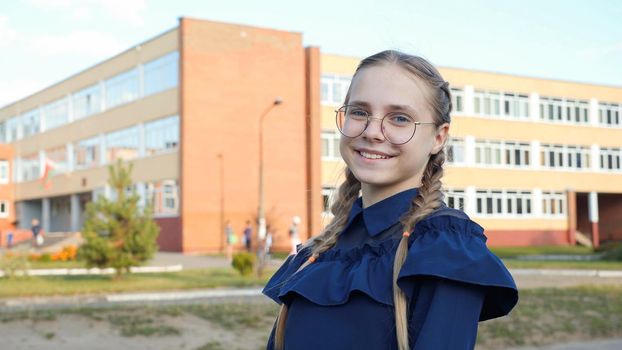 A teenage girl wearing glasses in front of a school