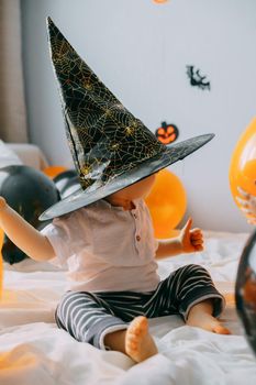 Children's Halloween - a boy in a witch hat and a carnival costume with airy orange and black balloons at home. Ready to celebrate Halloween.