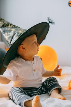 Children's Halloween - a boy in a witch hat and a carnival costume with airy orange and black balloons at home. Ready to celebrate Halloween.