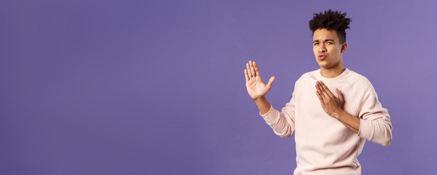 Portrait of funny and carefree young hispanic guy holding hands in martial arts attack pose, folding lips acting sassy and cool as imitating ninja, ready to defeat coronavirus, purple background.