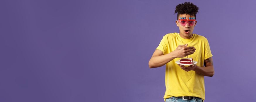 Celebration, party and holidays concept. Portrait of happy funny, enthusiastic young man celebrating birthday, protect lit candle on b-day cake from wind, making wish, smiling cheerful.