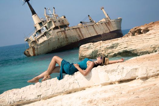 a young woman lies on a rock against the backdrop of Abandoned ship Edro III near Cyprus beach. Rusty ship ran on the ground near the shore. old stranded ship. paphos. Cyprus. Limassol.