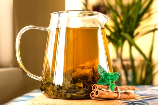 teapot of herbal tea with oranges, cinnamon sticks, healthy drink. The concept of natural herbal tea for weight loss. Fresh mint and large tea leaves on the wooden table with blurred light background