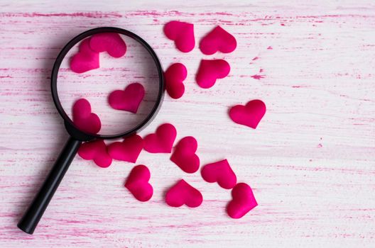 the heart lies under a magnifying glass, among many other hearts on a light wooden background. Love search concept. High quality photo