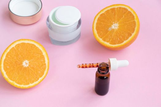 face serum, cream and orange on a pink background. Vitamin c concept in cosmetology and cosmetics. High quality photo