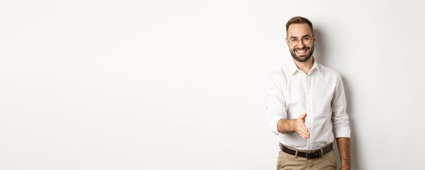 Confident businessman extending hand for handshake, greeting business partner and smiling, standing over white background.