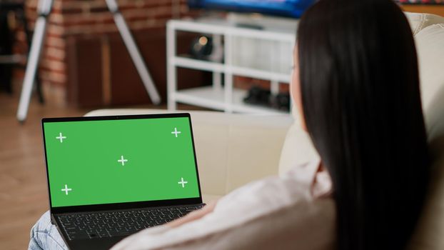 Person with computer having mockup isolated background while in apartment. Woman having laptop with green screen chroma key template display while sitting on sofa at home.