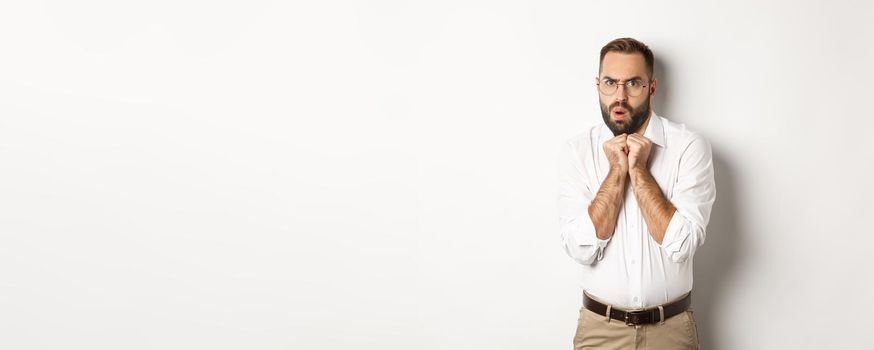 Scared and timid businessman looking anxious, trembling from fear, standing over white background.