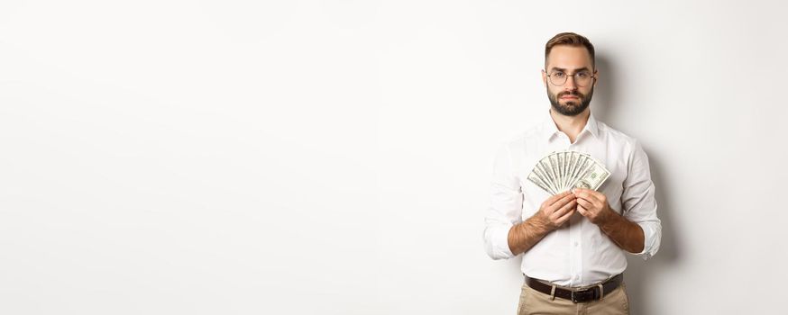 Serious businessman holding money, showing dollars, standing over white background.