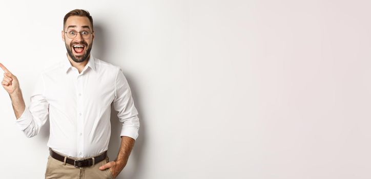 Surprised and excited man making announcement. Businessman pointing finger left at copy space, white background.