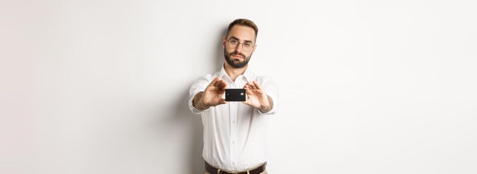 Serious businessman showing credit card, standing over white background.